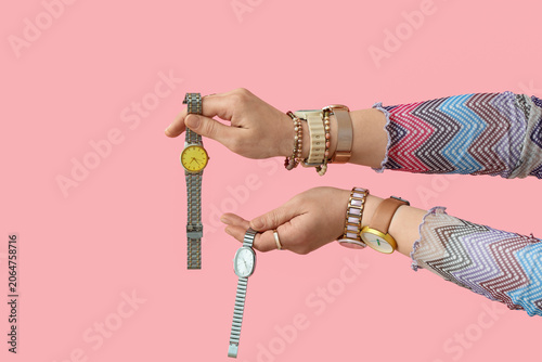 Female hands with stylish wristwatches and jewellery on pink background