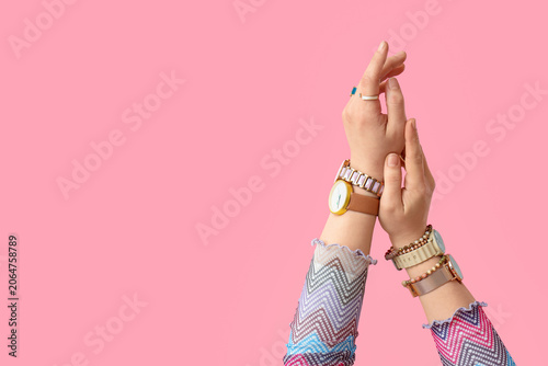 Female hands with stylish wristwatches and jewellery on pink background