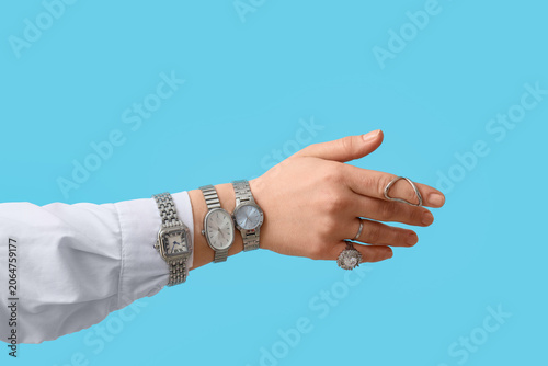 Female hand with different stylish wristwatches on blue background