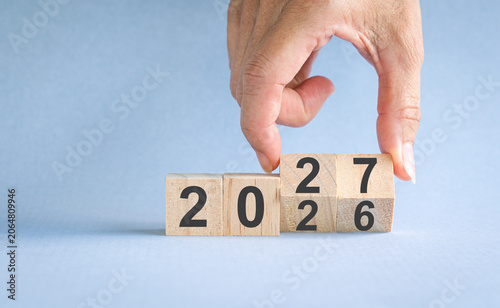 Hand turning wooden blocks from Year 2026 turn to 2027. New year concept.