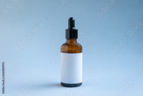 Amber Dropper Bottle with Blank Label, isolated on light blue background.