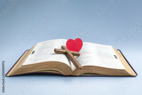 Open Bible with Cross and Heart Symbol, isolated on light blue background.