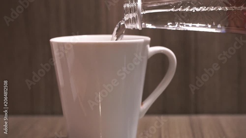 Clear water being poured from a glass bottle into a white ceramic cup. Concept of hydration, healthy lifestyle, refreshment, purity, wellness, and daily drinking habits.
