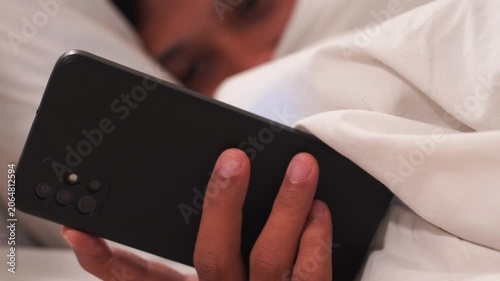 Man in bed at night using a mobile phone. A close-up shot of someone dealing with insomnia. Digital addiction, mental health, technology overuse.