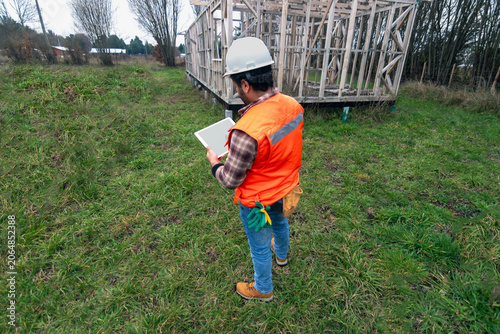 Construction supervisor using a digital tablet with a blank screen in front of a wooden house frame