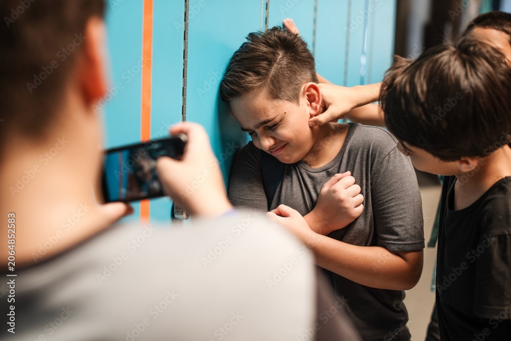 Obraz premium A boy is being bullied by peers in a school hallway near lockers.