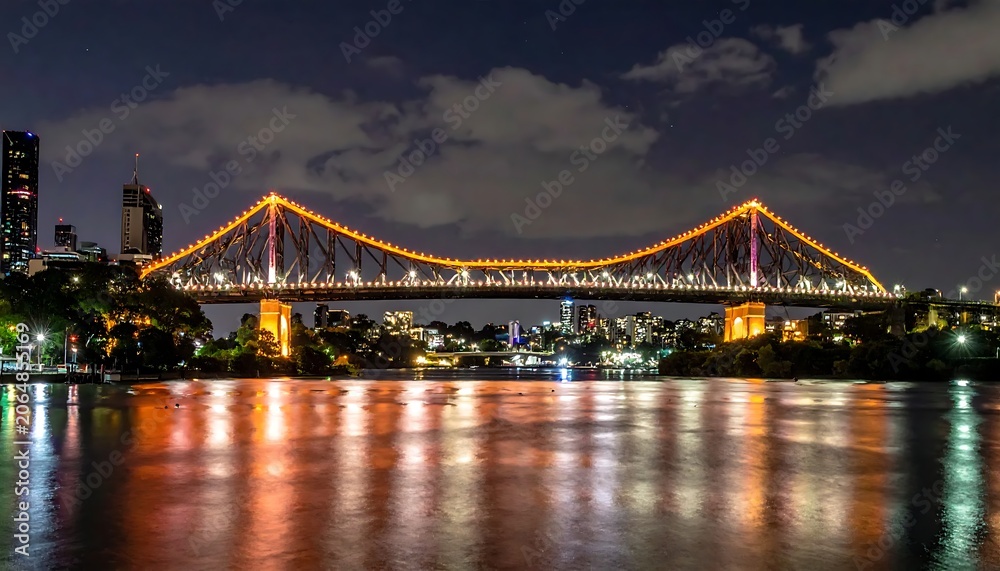 Fototapeta premium Illuminated Steel Bridge Spanning Calm River at Night in Urban Cityscape