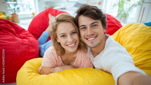 Happy couple taking a selfie on colorful bean bags in bright room