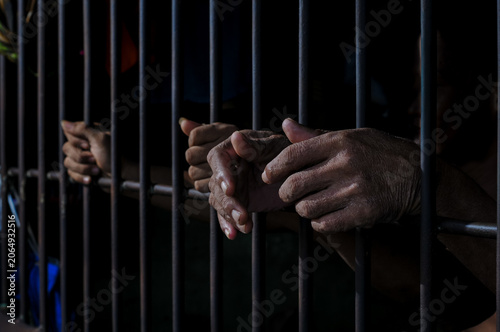 Fotografie prisoner's hands behind bars with black background