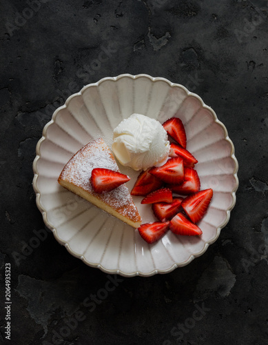 Delicious dessert - lemon cake with vanilla ice cream and strawberries on a dark background, top view