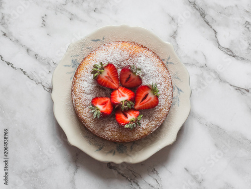 Lemon cake decorated with strawberries on a light marble background, top view
