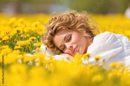 Serene Slumber in Dandelion Field: A young woman with blonde curly hair sleeps peacefully, nestled amidst a vibrant field of yellow dandelions.