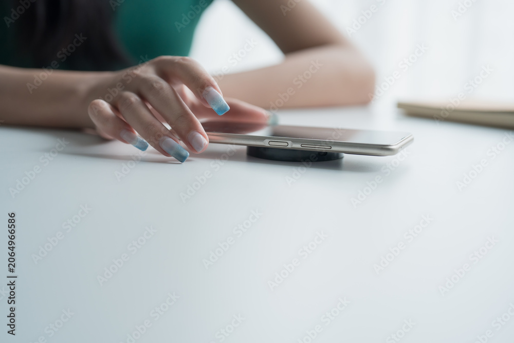 Fototapeta premium Charging mobile phone battery with wireless charging device in the table. Smartphone charging on a charging pad. Mobile phone near wireless charger Modern lifestyle technology.