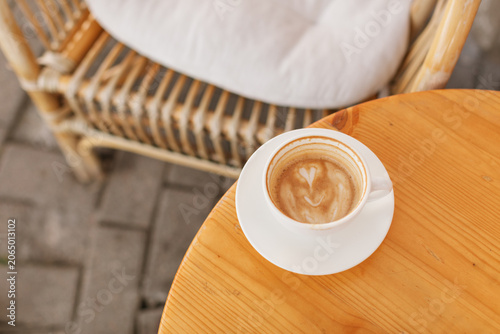 Overhead view of a coffee cup with a heart-shaped foam pattern at a summer sidewalk cafe terrace.