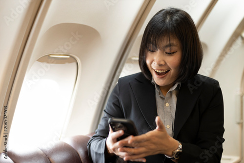 Foto Close-up of a surprised and smiling Asian businesswoman holding a smartphone beside an airplane window