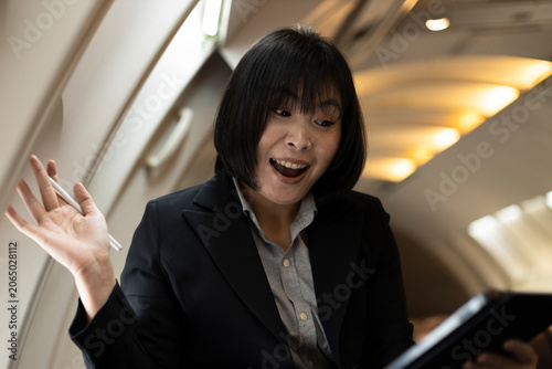 Bild auf Leinwand Close-up of a surprised Asian businesswoman holding a digital tablet in a private jet cabin