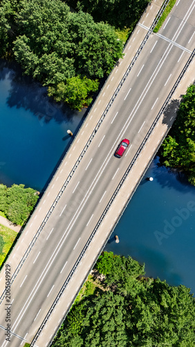 Aerial drone view of car crossing bridge over river, forest landscape and modern road bridge, transportation and infrastructure concept, the Netherlands, vertical image