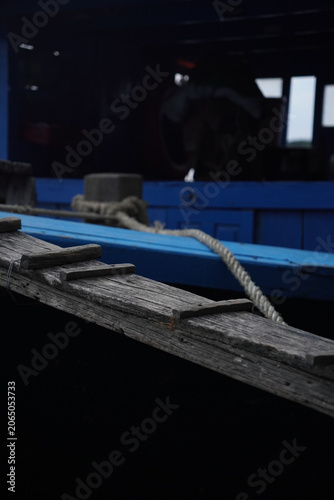 Obraz na plátně Close-up of old weathered wooden gangplank leading to blue fishing boat hull, da