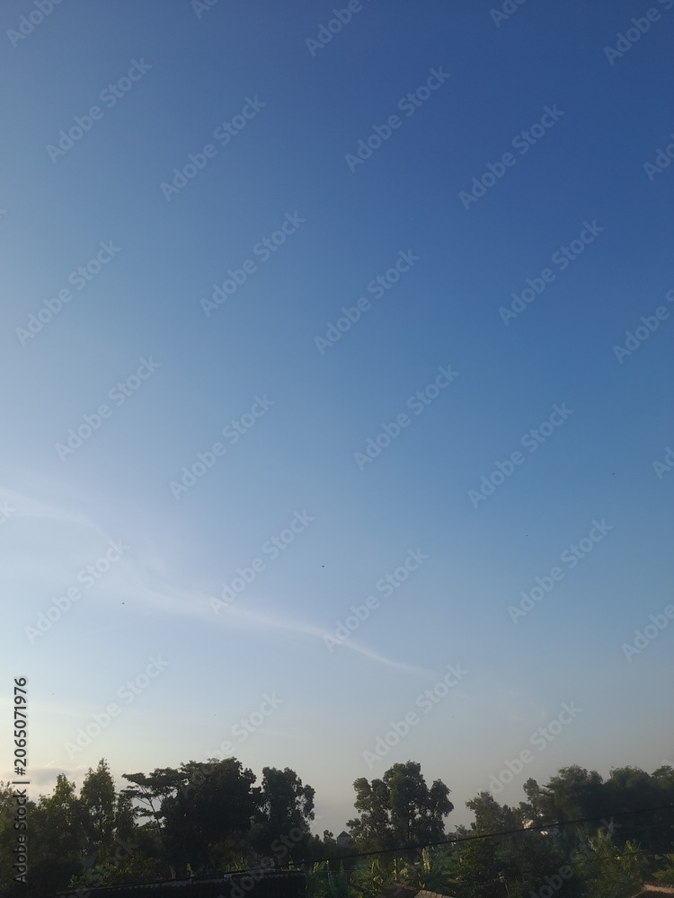 Obraz premium Beautiful and serene view of vast blue sky with white clouds and trees.