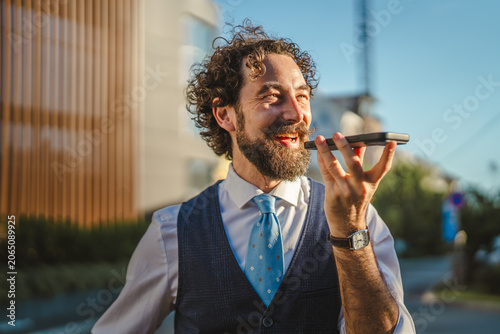 Quadro su tela Businessman talking on smart phone using voice assistant outdoors