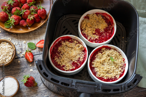 Homemade dessert traditional English crumble cake with strawberry in kitchen gadget modern air fryer on wooden background. Lifestyle trendy of new cooking.