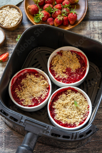 Homemade dessert traditional English crumble cake with strawberry in kitchen gadget modern air fryer on wooden background. Lifestyle trendy of new cooking.