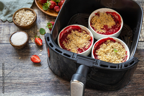 Homemade dessert traditional English crumble cake with strawberry in kitchen gadget modern air fryer on wooden background. Lifestyle trendy of new cooking. Copy space.