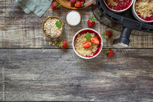 Healthy cooking with air fryer: homemade dessert traditional English crumble cake with strawberry on a wooden table. Top view flat lay background. Copy space.