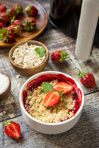 Healthy cooking with air fryer: homemade dessert traditional English crumble cake with strawberry on a wooden table.