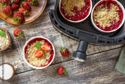Healthy cooking with air fryer: homemade dessert traditional English crumble cake with strawberry on a wooden table. Top view flat lay background.
