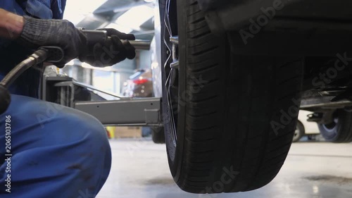 Close-up of a car mechanic unscrewing the bolts on a wheel with an electric screwdriver at a service station. Assembly and disassembly of wheels in a workshop. Repair and maintenance of a car.