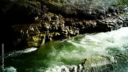 Foto Thick steam plumes billow from rugged canyon walls over a flowing river and a na