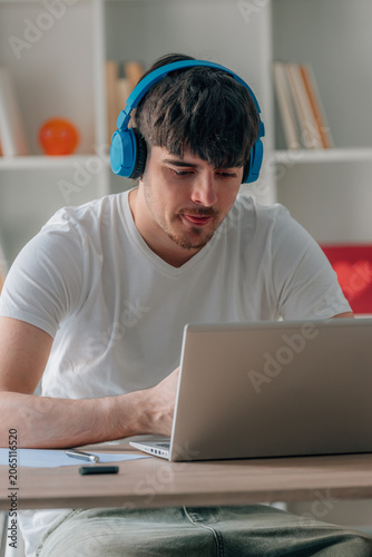 young man at home taking an online course with headphones and a laptop on his desk, studying and working with motivation and effort