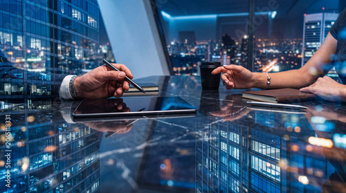 Fotografie Business professionals engage in a strategic night meeting, with a tablet reflecting a vibrant modern cityscape