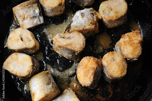 Fried fish pieces cooking in a cast iron pan with oil