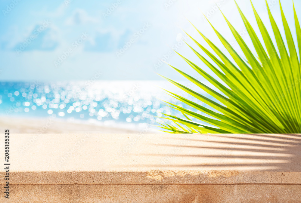 Obraz premium Stone table for placing product overlooking blurred seascape with tropical beach landscape and green palm leaves