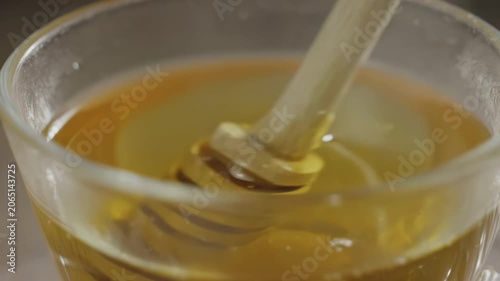 Honey dripping from wooden dipper into glass bowl, showcasing the smooth flow and texture of the golden liquid in a warm, inviting kitchen setting