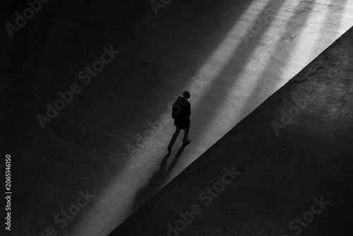 Cinematic black and white silhouette of lonely man walking through dramatic light beam symbolizing path, hope, and corporate leadership for advertising.