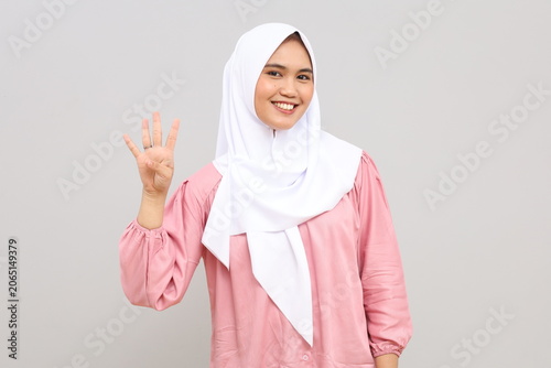 Obraz na płótnie A beautiful young Muslim woman wearing hijab on an isolated gray background, showing and pointing up with her finger the number four while smiling confidently and happily