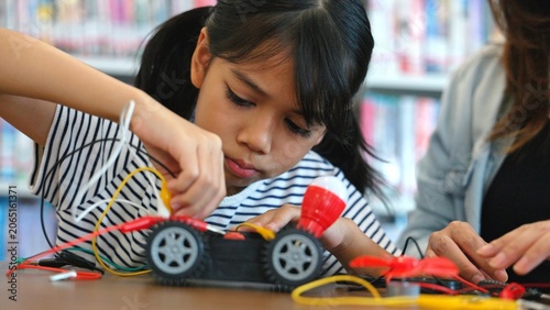 Tableau sur toile Clever Asian youth learner focusing on automated engineering mechanics task with guidance from female mentor