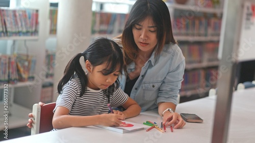 Creative young girl pupil drawing with pencil with guidance from female teacher at library table. Focused child student learning artistic literacy skill to expand smart mind.
