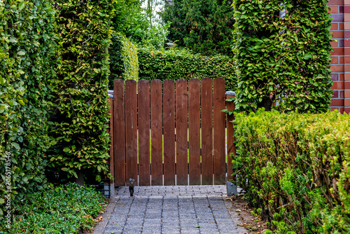 Foto A close-up view of a vertical brown wooden picket gate blocking a paved stone path between lush green garden hedges