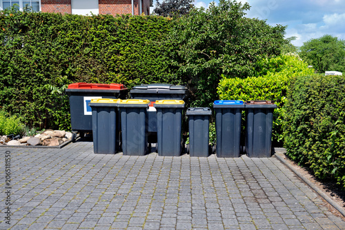 Bilde på lerret A neat row of various plastic garbage and recycling bins with colored lids standing on a paved driveway in Germany