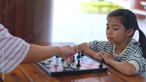 Fotografie Cute Asian girl child playing traditional chess board game attentively inside comfortable school library space
