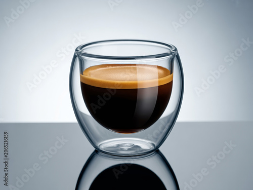Aromatic, freshly brewed espresso coffee showcased in a modern double-walled glass cup, highlighting its rich dark color and smooth crema on a reflective surface
