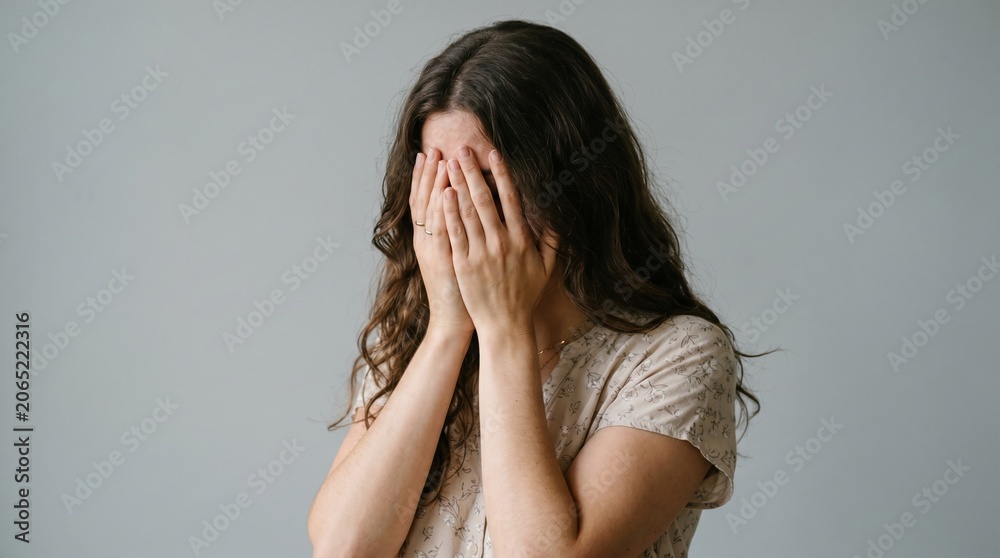 Fototapeta premium Young woman covering her face with hands in a sign of distress and sadness distress depression isolated suffering