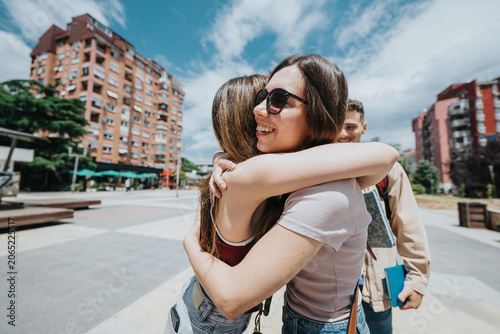 Slika na platnu Two female students embrace and smile while meeting in an urban campus plaza