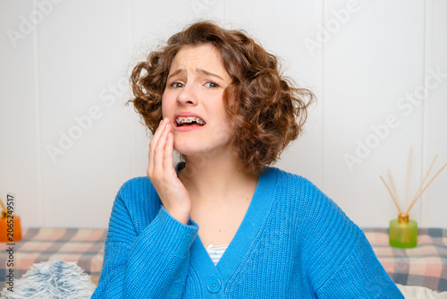 young woman with dental braces suffering from a toothache, holding her painful jaw with a distressed expression, highlighting oral health issues