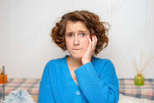 close-up portrait of a distressed young woman with curly hair, biting her lip and holding her cheek, expressing worry, pain, or deep thought