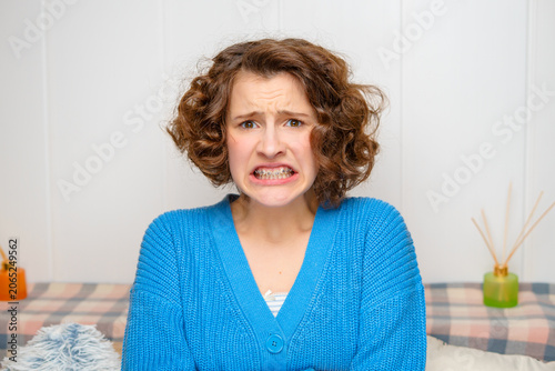 young woman with braces grimacing in discomfort, showing extreme frustration and stress on a plain white background
